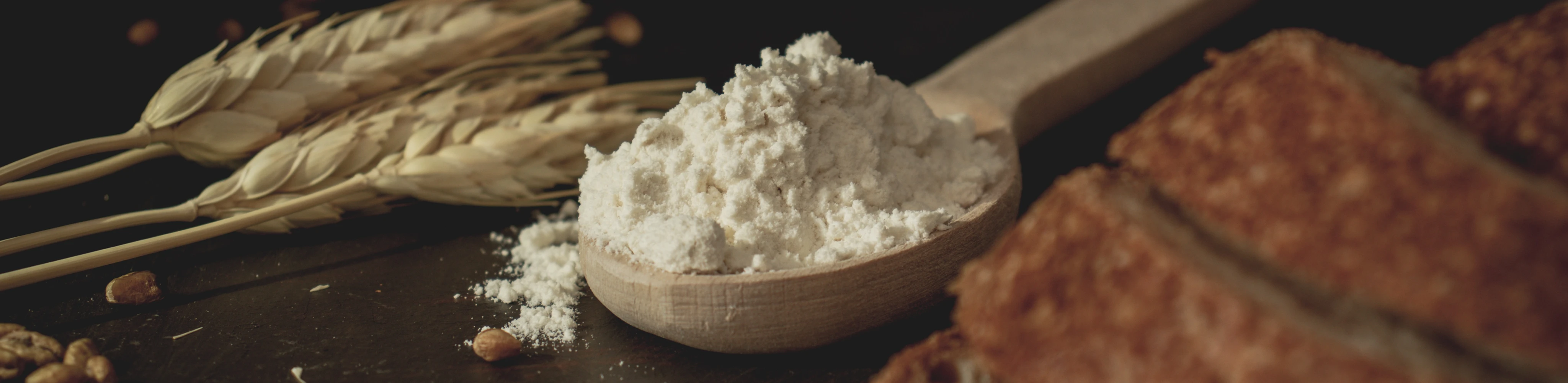 Ein Holzlöffel mit einem Haufen Mehl zwischen Getreide, Körnern und einem Brot