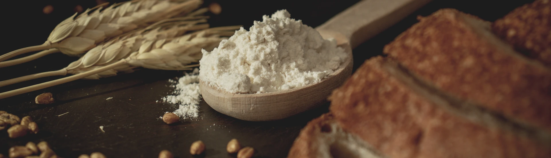 Ein Holzlöffel mit einem Haufen Mehl zwischen Getreide, Körnern und einem Brot